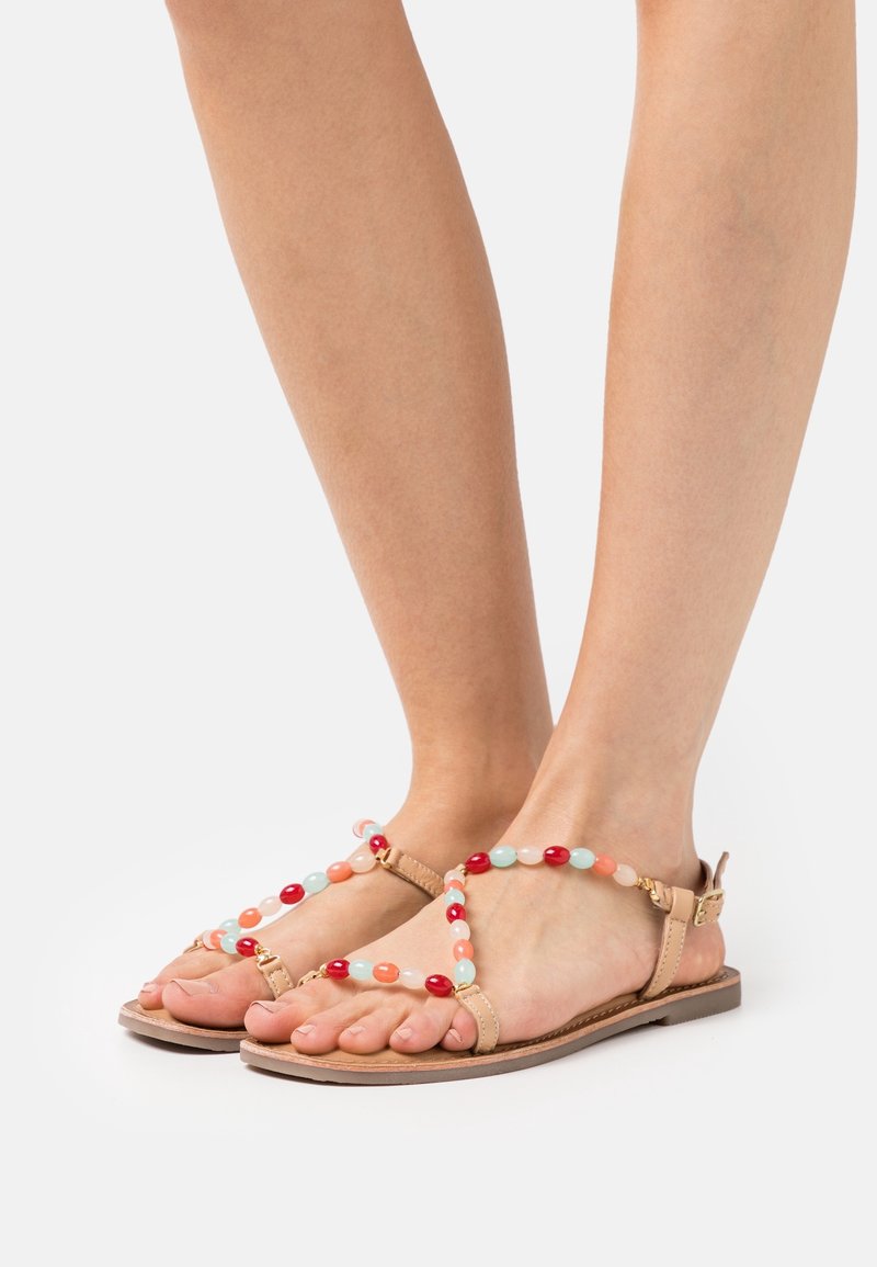 Plážové sandály s plochou podrážkou, vyrobené z hnědé kožené základny, s vícebarevnými korálky v červené, korálové a zelené barvě na horních popruzích.