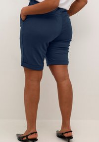 Shorts in cotone blu navy con un design attillato, con risvolti alle estremità e tasche laterali, abbinati a scarpe slingback nere. Texture liscia.