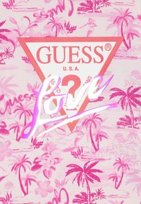 Fundal cu imprimeu tropical roz, cu palmieri și flori. Logo-ul triunghiular central roșu conține "GUESS U.S.A." și cuvântul "Love" în scris alb.