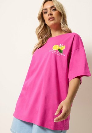 Blondynka w jasnoróżowej oversize koszulce z grafiką cytryny i napisem "Limone d’Italia" oraz jasnoniebieskich szortach jeansowych.