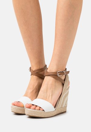 Hvide åben tå kilehælssandaler med en flettet jutesål og brune ankelstropper. Har et krydsbåndsdesign for ekstra støtte.