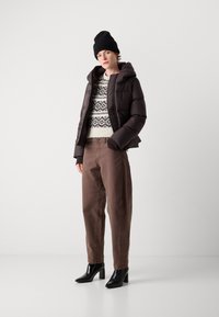 Doudoune matelassée marron avec capuche, pull crème léger avec un motif noir, chinos marron et bottines à talons noires.