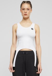 Biela bavlnená crop top s okrúhlym výstrihom a bočnými výrezmi, s malým čiernym logom na ľavej hrudi.