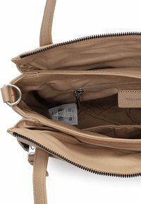 Beżowa torebka o fakturowanej powierzchni, wyposażona w komory zapinane na suwak, materiałową podszewkę oraz srebrzysty pierścień jako ozdobę.