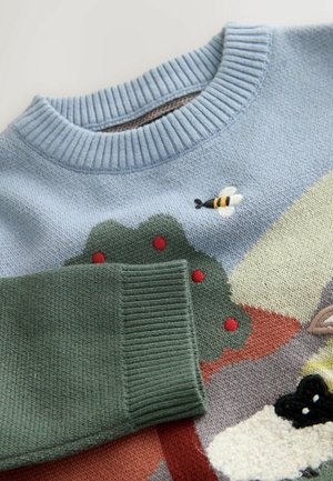 Stickad tröja med en ljusblå bas, med en broderad bi och träd i gröna, röda och flerfärgade mönster på framsidan.