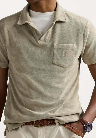 Polo en tissu éponge beige, avec un col, des manches courtes et une poche poitrine avec un détail de logo subtil.