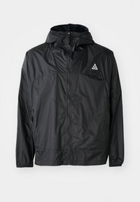 Veste légère noire en nylon. Dotée d'une capuche, d'une fermeture éclair intégrale, de poignets élastiques et d'un logo triangulaire sur la partie supérieure de la poitrine.