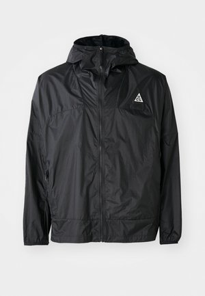 Veste légère noire en nylon. Dotée d'une capuche, d'une fermeture éclair intégrale, de poignets élastiques et d'un logo triangulaire sur la partie supérieure de la poitrine.