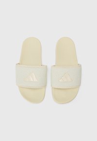 Cream slide sandals featuring a perforated strap, textured surface, and an embossed logo detail. Designed for comfort and ease of wear.