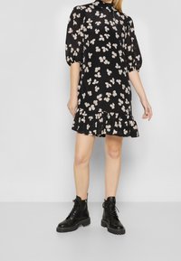 Černé šaty s krátkými nabíranými rukávy, květinový potisk v světlé béžové, volánkový lem, lehká tkanina. Nosit s černými šněrovacími kotníkovými botami.