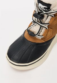 Botte d'hiver avec un orteil en caoutchouc noir, un dessus en daim marron, une doublure en laine polaire blanche et des lacets noir et blanc avec des cordons en plastique.