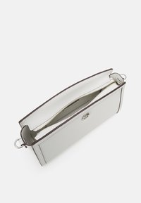 Šedá kožená kabelka s hladkou texturou, horním zipovým uzávěrem, béžovou podšívkou a kovovým akcentem loga na přední straně.