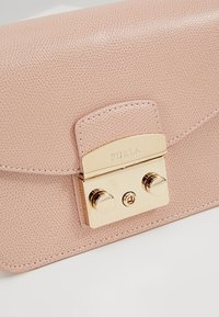 Borsa in pelle testurizzata rosa chiaro con una chiusura in metallo dorato incisa con "Furla" e due pomelli cilindrici sul davanti.