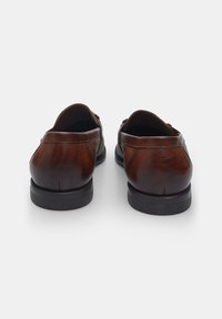 Pruunist nahast slip-on kingad sujuva viimistlusega, polsterdatud sisetallaga, ümarate varvastega ja musta kummitaldaga, millel on peened õmblusdetailid.