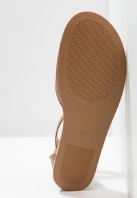 Ruskea sandaalin pohja, jossa on uritettu pinta ja koko 37 -merkintä. Materiaali näyttää joustavalta, täydentäen yksinkertaista narumallista muotoilua.