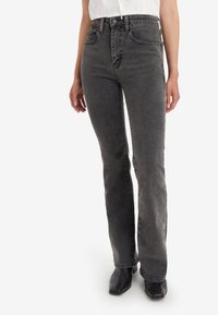 Jean en denim gris évasé à taille haute, avec cinq poches, détails de couture et une texture légèrement délavée. Porté avec des bottines noires.