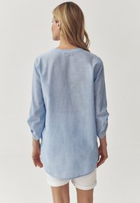 Camicia azzurra chiara, con maniche lunghe e scollatura rotonda, design casual e orlo leggermente curvo, realizzata in un tessuto morbido e testurizzato.