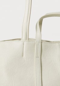 Biała skórzana torba tote o teksturowanej powierzchni. Posiada dwa solidne uchwyty i widoczne szycie wzdłuż krawędzi. Prosty, prostokątny design.