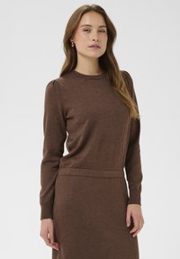 Rjav pleten pulover z dolgimi rokavi, okroglo izrezano ovratnikom in rebrastimi manšetami. Gladka tekstura z nežnimi naborki na rami.