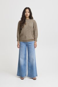 Maglione marrone lavorato a maglia con motivo testurizzato, abbinato a jeans di denim azzurro chiaro a gamba larga. Sandali neri con tacco completano l'outfit.