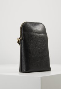 Svart pebblemönstrad läder crossbody-väska med guldblixtlås och metalldetaljer, stående upprätt på en vit yta mot en neutral bakgrund.