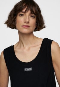 Zwart mouwloos topje met een ronde halslijn, voorzien van een label met de tekst "10 DAYS" aan de voorkant. Gladde stof en minimalistisch design.