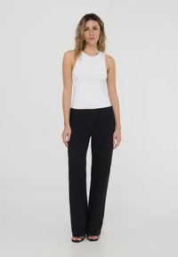 Top bianco senza maniche con un motivo testurizzato, abbinato a pantaloni neri a gamba dritta. L'outfit presenta un design semplice e aderente, con colori neutri.