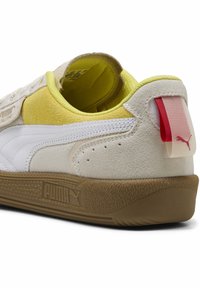Hvide og gule ruskinds sneakers med en gummisole, der har en rød og hvid pull-tab og teksturerede detaljer på overdelen.