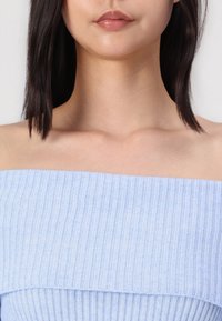 Top azzurro chiaro scollato sulle spalle realizzato in tessuto a costine, con un ampio scollo e una consistenza morbida, che mette in mostra le spalle e la clavicola.
