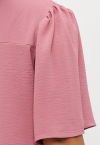 Pink short-sleeve top with a textured finish, featuring puffed sleeves and a wide neckline. Soft fabric with subtle ripples throughout.