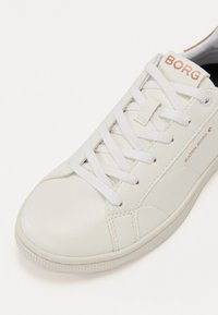 Hvite lær sneakers med hvite lisser, avrundet tå og strukturert gummisåle. "BORG"-logo i oransje på tungen.