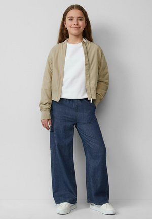 Beige bomberjack, witte T-shirt, wijde donkere denim broek en witte sneakers. Glad materiaal en casual pasvorm.