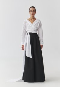 Witte wikkelblouse met lange mouwen, gecombineerd met een zwarte, high-waisted rok. De outfit heeft een strikdetail en zachte texturen.