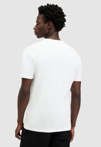 T-shirt bianca in cotone con maniche corte, colletto tondo e orlo dritto, caratterizzata da una texture liscia. Modello mostrato da dietro.