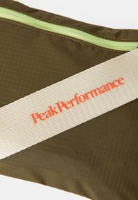 Smeđa platnena torbica s zelenim patentnim zatvaračem, koja ima teksturiranu krem traku označenu s "PeakPerformance" u svijetlo narančastoj boji.