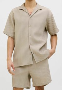 Lichtbeige shirt met korte mouwen, verticale strepen en een kraag, gecombineerd met bijpassende korte broek. Knopen zichtbaar op het shirt.