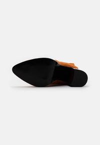 Scarpa con tacco in suede color arancio bruciato, con punta affusolata e suola nera liscia con texture scanalata per una presa migliore.