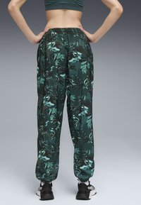 Grønne camo-joggers med elastisk talje, løs pasform og indsnørede manchetter. Fremstillet af letvægtsstof med en blank tekstur og abstrakt bladmønster.