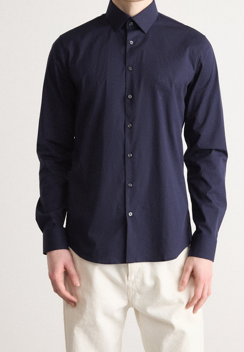 Donkerblauwe langermige blouse met knopen, gemaakt van een gladde stof, met een klassieke kraag, knoopsluiting en een getailleerde pasvorm.