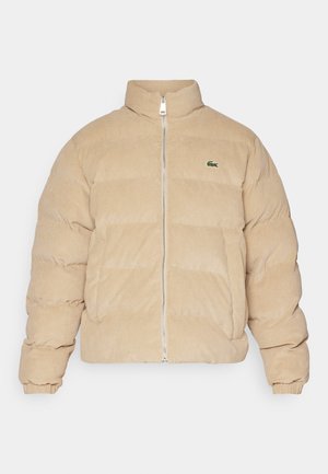 Beige corduroy puffer jack met een hoge kraag, ritssluiting en geribde manchetten. Beschikt over een gestikt patroon en een klein geborduurd logo.