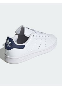 Sneaker Adidas Stan Smith bianca con tallone blu navy, strisce laterali perforate, lacci bianchi e logo stampato sulla suola.