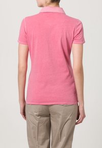 Polo shirt in cotone rosa con colletto e maniche corte, caratterizzato da una texture liscia e dettagli di cucitura discreti.