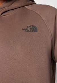 Felpa in cotone marrone con cappuccio, caratterizzata da un logo scuro di "The North Face" sulla parte sinistra del petto. Tessuto morbido e maniche aderenti.