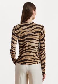 Langsleeve top in tan met zwarte tijgerstrepen. Zachte textuur, aansluitende silhouet, ronde hals en zijsplitten aan de onderkant.