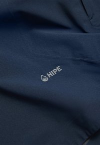 Tessuto impermeabile blu navy con una texture sottile; presenta un logo grigio chiaro con la scritta "HIPE" vicino a una cucitura.