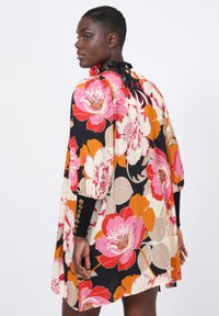 Geprinte jurk met grote bloemenpatronen in roze, oranje en crème op een zwarte achtergrond, met een relaxed fit en knoopmanchetten.