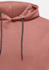 Sudadera de algodón en color rosa polvo con capucha ajustable mediante cordón. Presenta una textura suave y cordones negros en contraste para su ajuste.