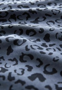 Tessuto con stampa leopardata caratterizzato da uno sfondo azzurro chiaro con forme nere organiche. Texture morbida con una leggera lucentezza, apparenza leggermente stropicciata.