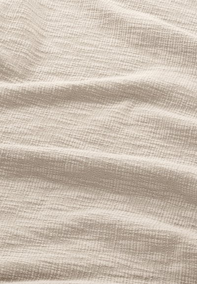 Lys beige tekstureret stof med subtile vævede mønstre, der har en blød, krøllet overflade og varieret overfladedybde.