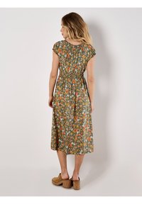 Grünes Blumenkleid mit kurzen Puffärmeln, gerafftem Bund und knielanger Länge. Es hat orangefarbene und weiße Blumen auf einem strukturierten Stoff.